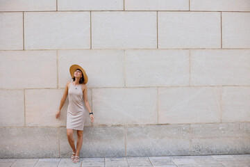 Young beautiful smiling girl in a trendy summer dress. Sexy carefree woman posing on the street against the wall in a hat.