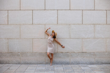 young girl posing near the wall. A girl in a beautiful dress and hat is having fun on the street standing near the wall. - 784926857