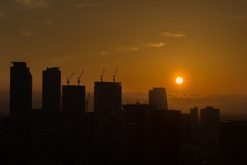 The sun is setting over a city skyline, casting a warm glow over the buildings tokyo metropolis...
