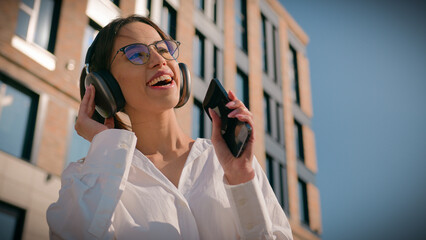 Happy asian woman businesswoman business lady female student listening music sing in headphones using mobile phone outdoors near office building joyful girl listen enjoy song singing moving dancing