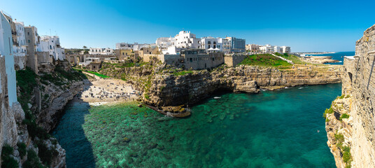 Wide panorama of Polignano a mare, a beautiful city in Puglia, italy, on a sunny day. Visible beach coming to the sea, looking from the old town next to it. Magical spring colors