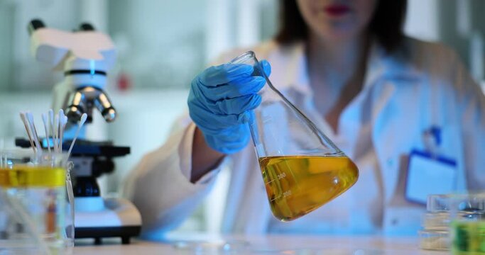 Scientist hands in gloves hold sterile flask with yellow liquid
