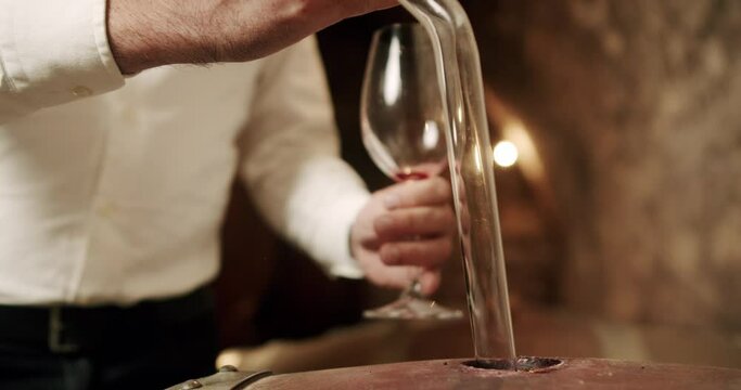 Using his hand, the man gracefully pours the liquid from the wood barrel into the glass, his fingers delicately gripping the tableware as his thumb controls the flow