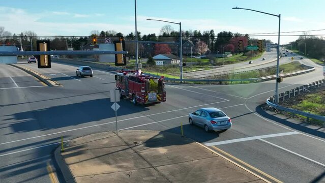 American Fire Engine crossing junction in city with waving Flag of USA on top. Sunset time in Suburb district of american town.Aerial tracking shot.