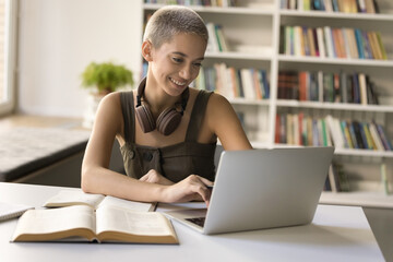 Pretty student girl sit at desk with laptop, watching webinar, preparing for exams or university...