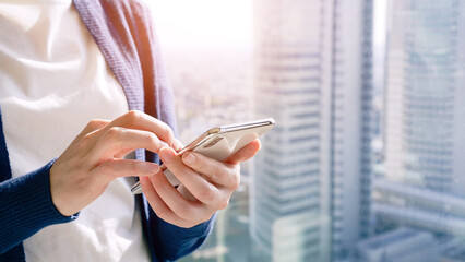 A woman operating a smartphone with the city in the background.