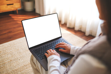 Mockup image of a woman working and typing on laptop computer with blank white desktop screen at...