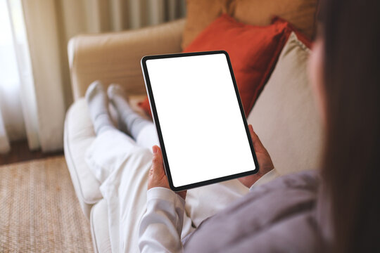 Mockup image of a woman holding digital tablet with blank desktop screen while sitting on a sofa at home