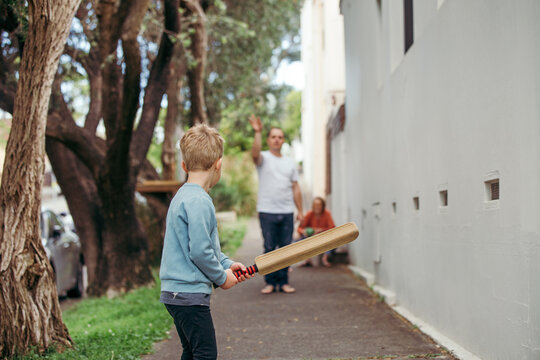 Shot from behind of young boy playing cricket in the street with his family