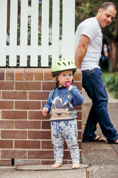 Young boy eating ice cream on suburban footpath with dad watching