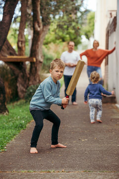 Boy playing cricket on footpath with family in background