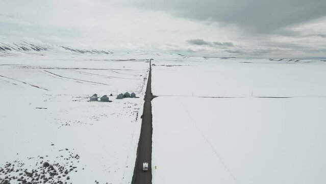 Aerial view trails a white camper van traversing a wintry, desolate landscape in Idaho, USA. Embracing the ethos of travel and exploration, journeying through the natural expanses. Vanlife concept.