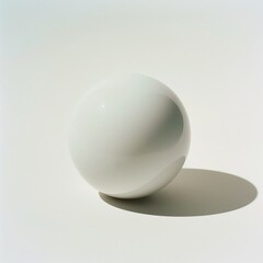A single glossy white sphere casting a soft shadow on a light surface, evoking simplicity and balance.
