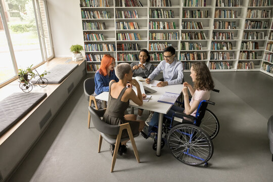 Overhead view students and girl in wheelchair take part in teamwork or educational seminar, literary club participants talking in library. Education, study accessibility for people with disabilities