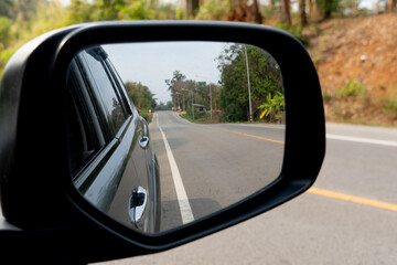 Reflection of the road in the side mirror of a car. Rear view mirror of car on asphalt road background. Copy space and blurred of roads in provincial areas