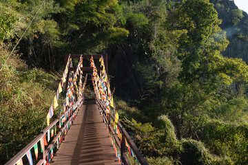 Wooden bridge in the middle of the forest with colorful prayer flags. At Wat Chaloem Phra Kiat...