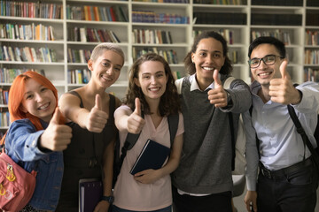 Group of multiethnic students posing in library showing thumbs-up gesture, sign of approval, agreement or satisfaction. Excellent, effective study, gaining new knowledge and education, choice meaning - obrazy, fototapety, plakaty