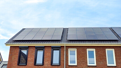 Fototapeta premium Newly built houses with black solar panels on the roof against a sunny sky Close up of new building with black solar panels. 