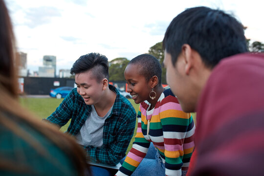 Group of young university students hanging out sitting on grass studying and using devices