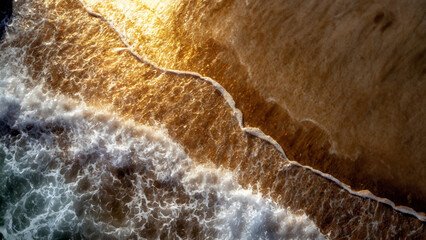 Aerial view of waves crashing on a sandy shore, creating white foam patterns