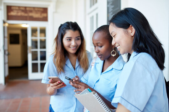 Three High School friends laughing whilst checking their mobile phones - Powered by Adobe