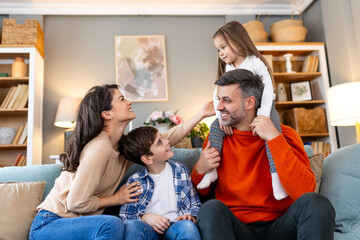Cheerful son and daughter sitting with parents playing at home. Playful little boy and girl enjoying spending time with parents at home.