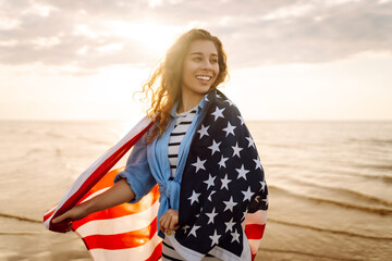 Woman patriot  with american flag on the beach at sunset. USA celebrate 4th of July. Independence...