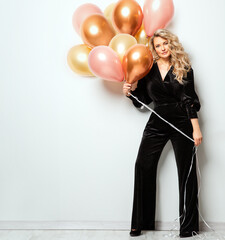 Beautiful Woman with Balloons over White background. Birthday Party Time. Fashion Model with Curly Hairstyle in Black Suit - 784998013