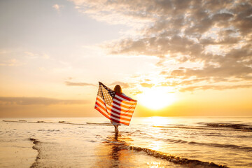 Woman patriot  with american flag on the beach at sunset. USA celebrate 4th of July. Independence Day concept