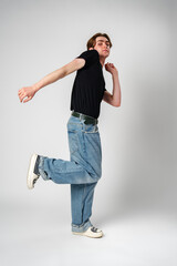 Young Man Performing a Casual Dance Move in Jeans and Sneakers Against a Grey Background