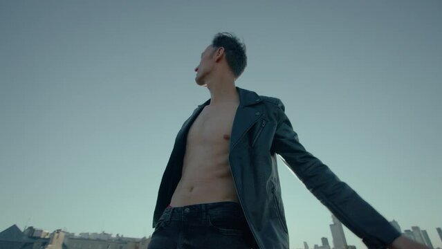 Young caucasian man dances on roof with city skyline in background