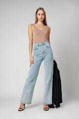 Young Woman Wearing High Rise Jeans and Tank Top posing on gray background in studio