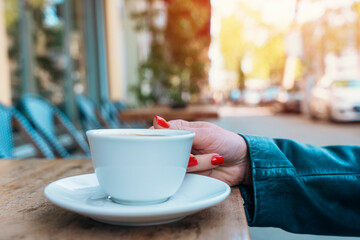 hand of woman holding white single cup of coffee in a street cafe