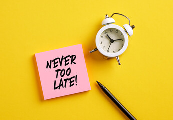 Never too late message on pink note paper with alarm clock and pen. Motivational message for taking action in business or life