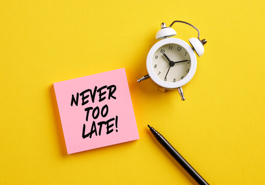 Never too late message on pink note paper with alarm clock and pen. Motivational message for taking action in business or life - Powered by Adobe