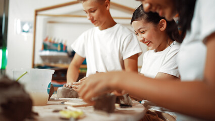 Handsome student dipping hand in to water to soften clay at art classroom. Group of diverse...