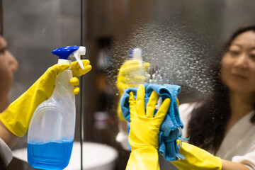 Cleaning service concept. Close up of female hands in yellow gloves cleaning mirror