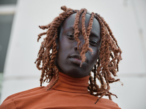 South Sudanese man wearing orange turtleneck looking down