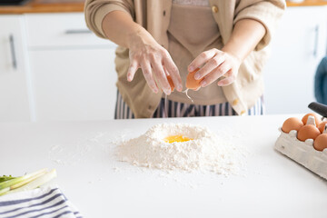 cropped shot of woman preparing dough with flour and egg on kitchen table. Woman preparing...