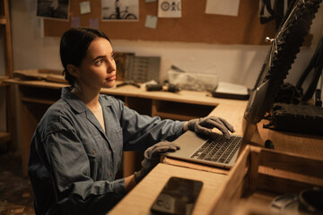 Woman bicycle mechanic is repairing a bike in the workshop, using laptop computer searching information. Bike service.