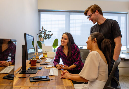 Three office workers looking together at a computer screen in an office