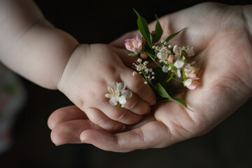 Mother's hand holding her baby's hand with flower, bonding between mom and child. - 785022228