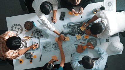 Top view of smart engineer team in casual cloth talking about turbine engine structure at table...