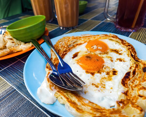 Roti sarang burung, a pratha looks like bird nest with half cook eggs in the middle served with teh tarik as staple breakfast in Malaysia.