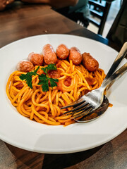 Hot dog or sausage with spaghetti in tomato sauce in white plate. Top view