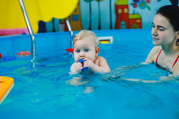 Fototapeta na wymiar A little boy of 9 months is learning to swim in the pool with a coach.