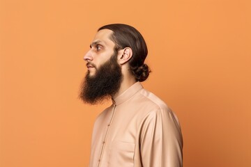 A man with a beard and a long ponytail is standing in front of a yellow wall