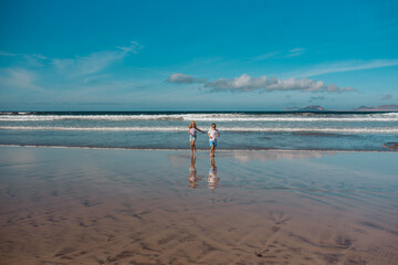 Siblings playing on beach, running, skipping in water. Smilling girl and boy on sandy beach of Canary islands. Concept of family beach summer vacation with kids.