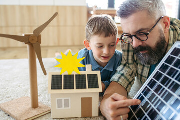 Father explaining renewable energy, solar power and teaching about sustainable lifestyle his young son. Playing with model of house with solar panels.