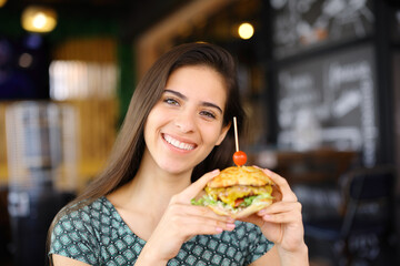 Happy woman looking at you showing burger in a bar